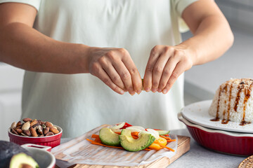 Woman preparing spring rolls in rice paper on kitchen table.