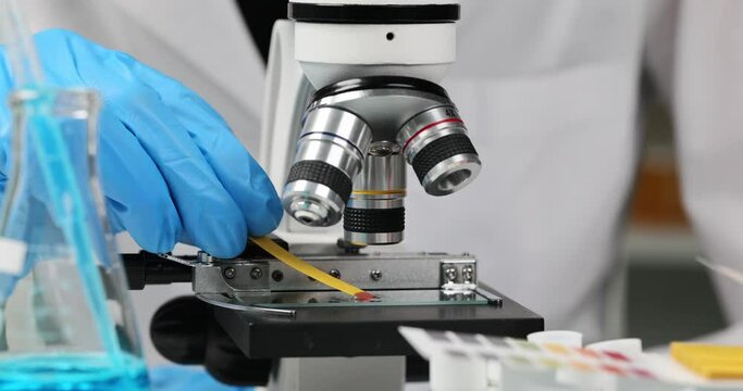 Scientist chemist checking acidity of liquid on glass slide near microscope using litmus paper closeup 4k movie slow motion. Chemical experiments concept