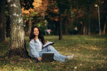 woman under tree with laptop and notepad