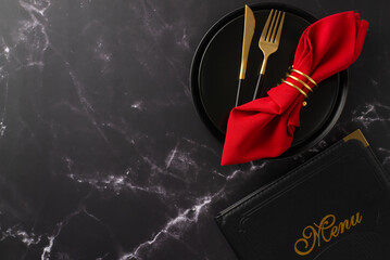 New Year's Eve dinner at a restaurant. Overhead shot of celebratory plates, elegant silverware, red napkin with ring, menu card on a glamorous black marble table with space for text or advert