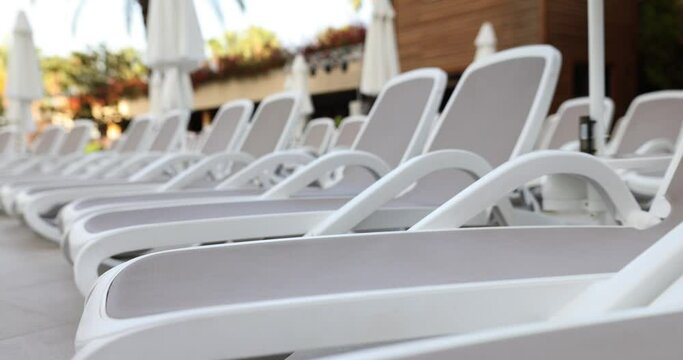 Empty sun loungers standing on edge of swimming pool 4k movie. Holidays at resort concept