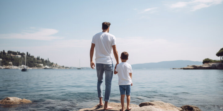 Dad and son in white t-shirts looking out to sea, back view