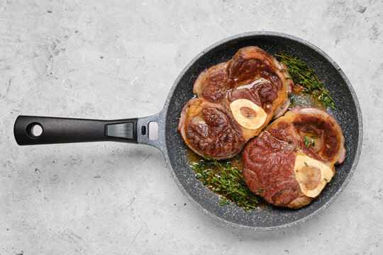 Two pieces of beef ossobuco in a frying pan with thyme