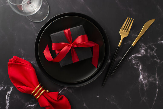 Christmas Eve Dining At A Restaurant. Overhead Shot Of Festive Plates With Present Box, Ornate Gold Cutlery, Holiday-themed Napkin With Ring, Wine Glass On A Beautiful Marble Table