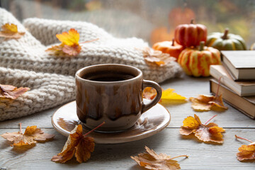 Autumn mood, autumn atmosphere. A cup of coffee, pumpkins, knitted warm blankets, books, autumn leaves on the windowsill.