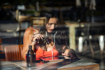 View through the window of a woman using digital tablet while relaxing in a coffee shop.