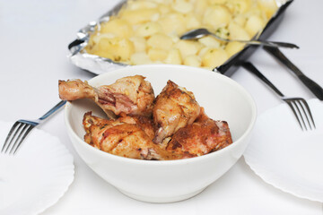 Chicken legs with potatoes recipes. Cheap dinner idea background. Simple dinner from Poland. Roasted chicken in bowl. White plates and tray of potatoes.