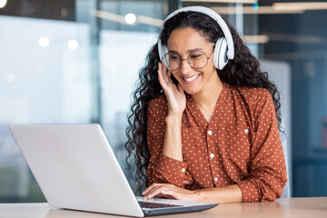 Young beautiful woman in headphones working with laptop inside office at workplace, joyful and...