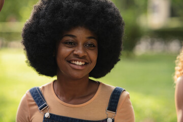 Fototapeta premium pretty african american woman with curly hair smiling in the park