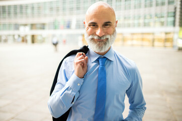 Mature bald stylish business man portrait with a white beard outdoor holding his jacket