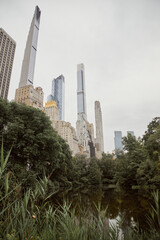 Fototapeta premium scenic view of trees and lake against modern skyscrapers in new york city, autumnal metropolis scene