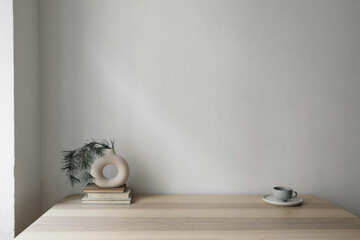 Modern vase on old books with pine tree branches.Cup of coffee on beige table.Empty white wall...