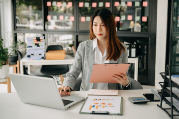 Fototapeta premium Woman freelancer is working her job on computer tablet and laptop Doing accounting analysis report real estate investment data, Financial at office.