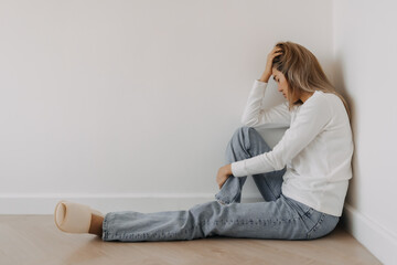 Asian Thai woman sitting on floor and leaning on white wall alone in apartment room. serious hopeless and upset disappointed. gloomy depression in winter. - obrazy, fototapety, plakaty