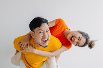 Happy Thai asian couple lover wear orange and yellow, woman riding piggyback on man back. Smiling...
