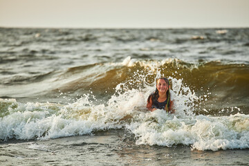 Little girl playing with waves in the sea. Kid playfully splashing with waves. Child jumping in sea waves. Summer vacation on the beach