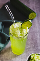 Detox cucumber lemonade in a glass with a straw and a cucumber on the table vertical view