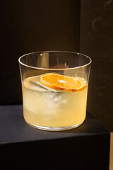 A refined cocktail based on brandy and rum, served in a Rocks glass, prominently displayed on a black podium; ideal for a minimalist menu