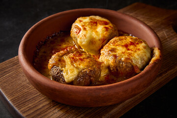 Close-up horizontal side view showcasing the intricate details of baked mushrooms, filled with rich suluguni cheese, presented on a Georgian clay plate 'keci'