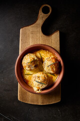 Vertical top view of baked mushrooms stuffed with meat, presented in a rustic clay plate on a wooden board, highlighting the essence of Georgian cuisine on a minimalist black background