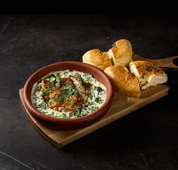 Side perspective in a square frame of satsivi, Georgian chicken in walnut sauce, elegantly laid out with tandoor bread on a black table