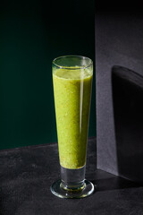 Green smoothie made of apple and kiwi in a glass, illuminated against a dark background with distinct shadows