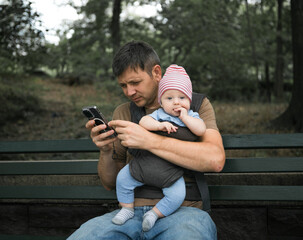 Father sitting on the bench and looking in the phone. Dad holding his baby son