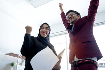 Muslim woman in hijab and Indian businessman celebrate success by tossing papers into the air after a successful transaction agreement, teamwork success concept