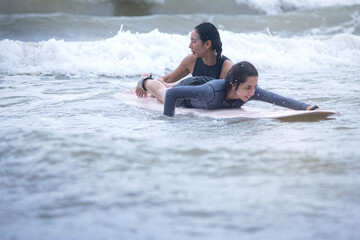 Pretty teenage girl learns to surf with a female instructor in the sea, extreme outdoor water sports