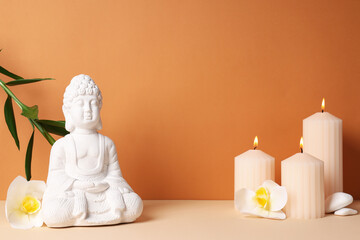 Buddha statue, candles, flowers and stones on orange background, space for text