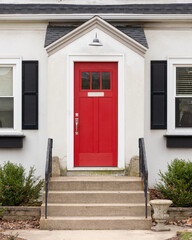 A red front door detail on a white home with concrete steps and iron railings leading up to the...