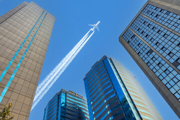 Airplane jet flying contrail above glass office buildings. Look up into the sky.