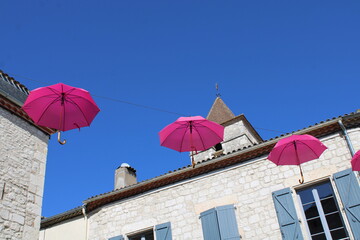 Fototapeta na wymiar Octobre rose, parapluies roses dans le village sous le ciel bleu