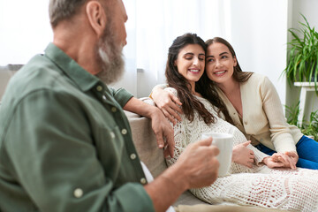 happy lgbt couple sitting on sofa and hugging, grey bearded man looking at his daughter, ivf concept