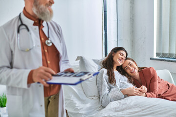 Obraz premium cropped view of doctor holding ultrasound with hugging lgbt couple on background, ivf concept