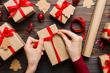 Woman is packing surprise gift for Christmas holidays, sitting at workplace with craft tools, top...