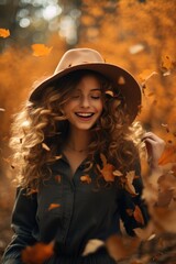 A happy woman in a hat and curly hair is smiling as the yellowing leaves fall. Autumn concept.