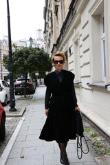 Dojrzała, elegancka kobieta na miejskim spacerze.
Kobieta w czerni. 