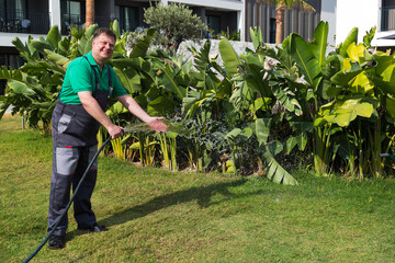 A blond man in work clothes waters the lawn near the house with a hose.