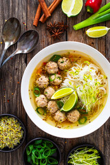 Oriental soup with meatballs, rice noodles and sprouts on wooden table