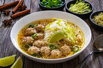 Oriental soup with meatballs, rice noodles and sprouts on wooden table