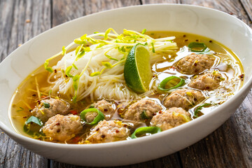 Oriental soup with meatballs, rice noodles and sprouts on wooden table