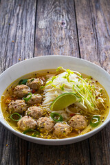 Oriental soup with meatballs, rice noodles and sprouts on wooden table
