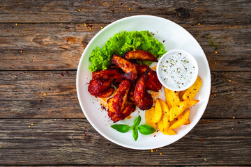 Buffalo wings with ranch dressing and French fries on wooden table
