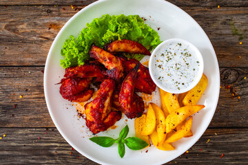 Buffalo wings with ranch dressing and French fries on wooden table
