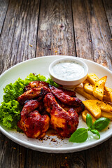 Buffalo wings with ranch dressing and French fries on wooden table
