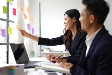 Businessmen and colleagues brainstorming scheduling business strategy, planning work in the office with paper stickers on the glass.