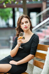 Beautiful young woman drinking white wine on the terrace of a restaurant. Relaxing after work with a glass of wine. Single woman having fun.