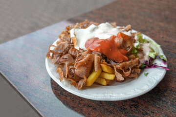 Doner kebab plate with meat, French fries, salad and two sauces served in a Turkish fast food restaurant in Germany, copy space, selected focus