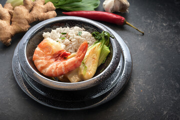 Tiger prawn or shrimp with pak choi and rice in a black ceramic bowl on a dark background, copy space, selected focus